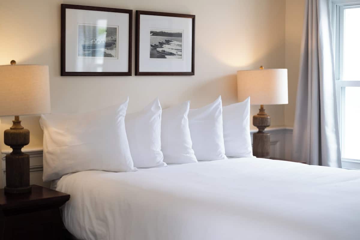 A neatly made bed with white linens and pillows, two framed pictures on the wall, and two bedside lamps.