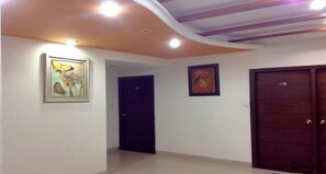 A hallway with a ceiling that has a curved design and recessed lighting. There are two doors and a framed picture on the wall.