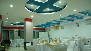 Une salle de banquet avec des tables rondes dressées pour le repas, des chaises blanches et un plafond orné de motifs bleus et blancs.