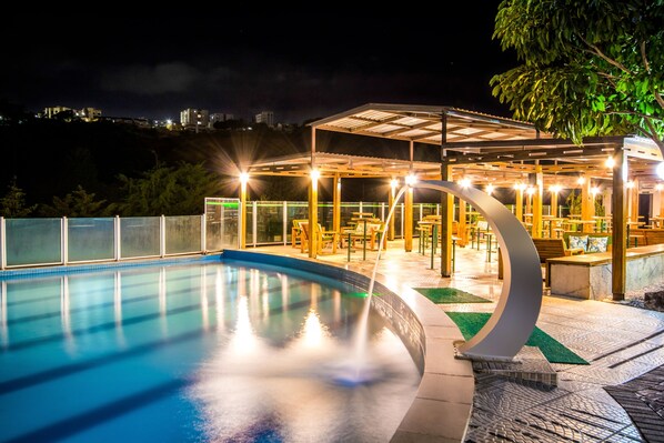 A swimming pool with a covered seating area and a view of a cityscape in the background.