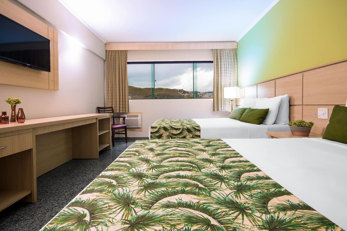 Hotelkamer met een bed, een bureau, een stoel, een televisie en een raam met uitzicht op heuvels.