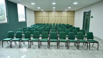 A conference room with rows of green chairs, a large window, and a door marked with an emergency exit sign.