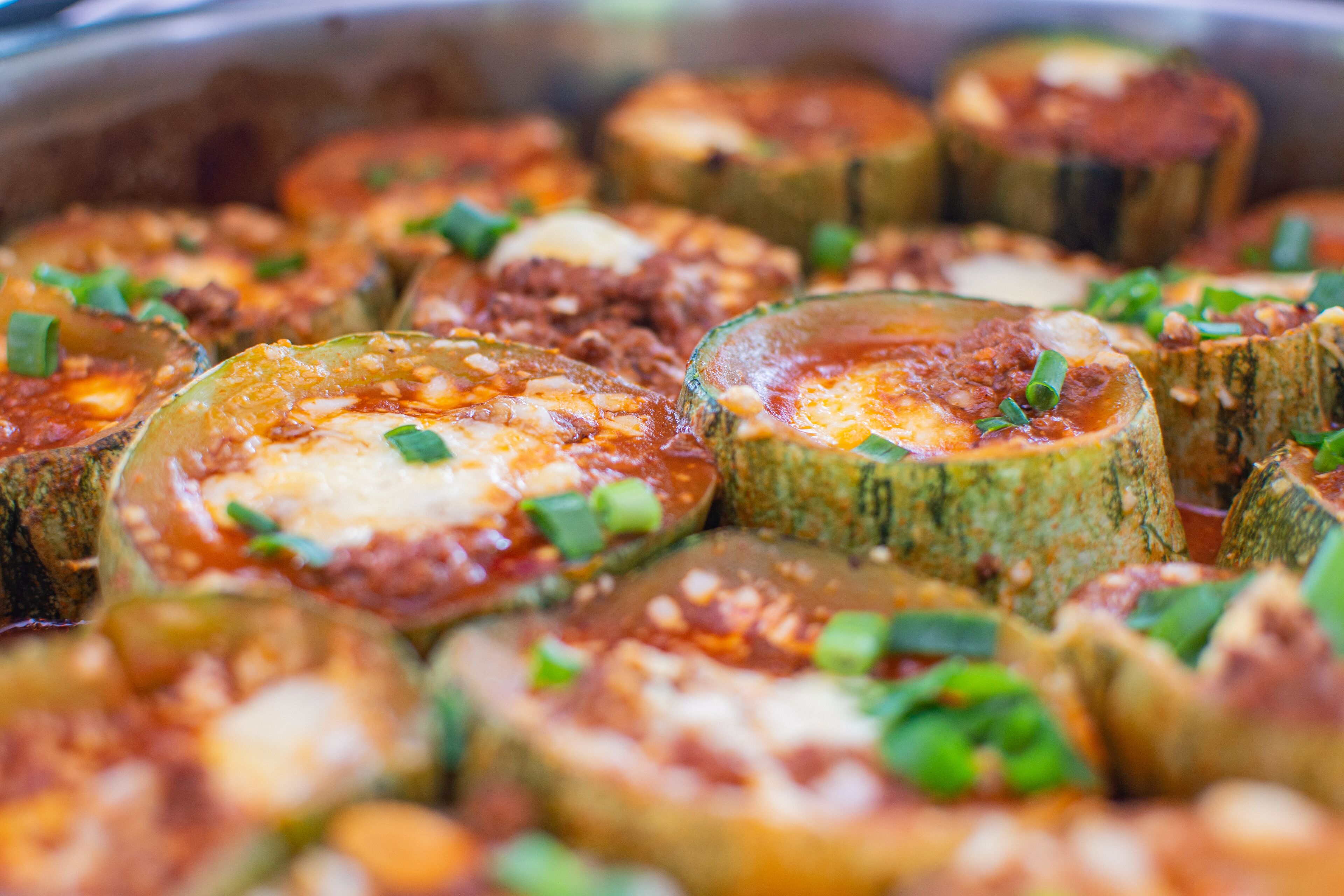 Een close-up van gevulde courtteslices met gesmolten kaas en rode saus, versierd met gehakte groene uien.
