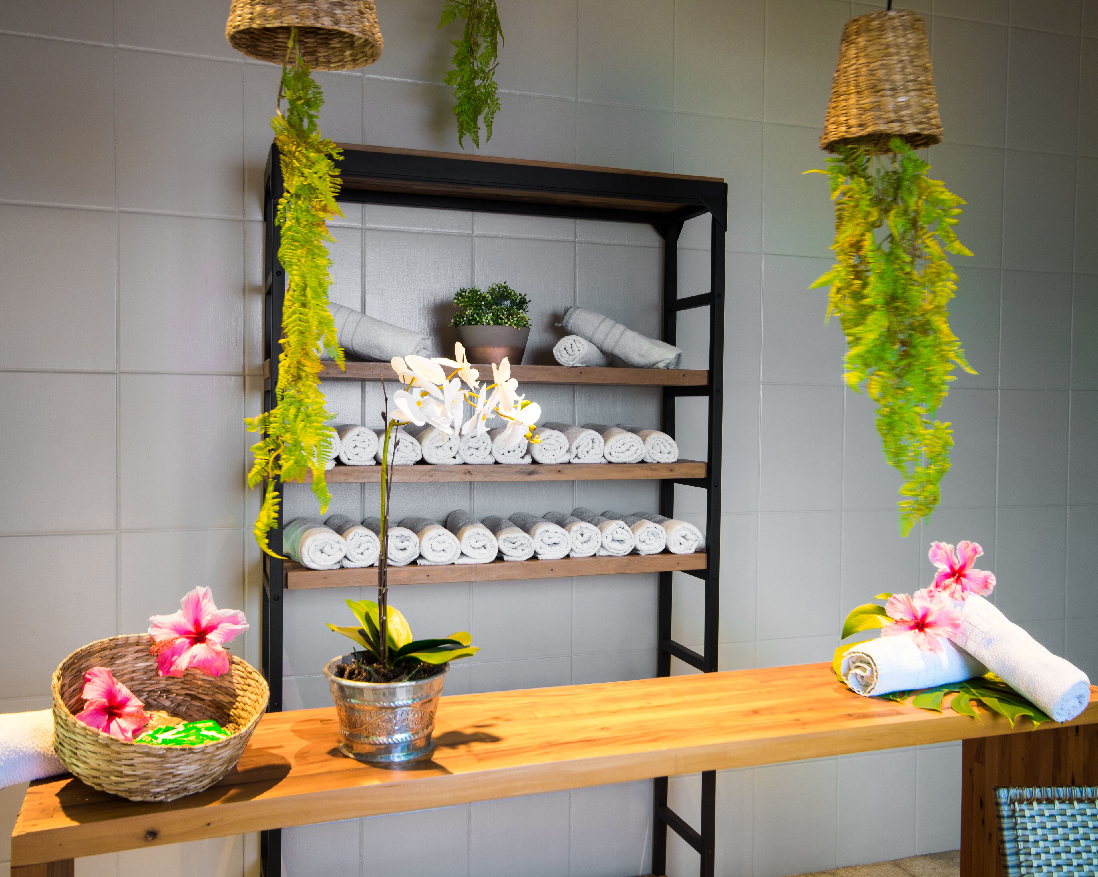 A wooden reception desk with a potted plant, rolled towels, and a shelf with neatly arranged towels.