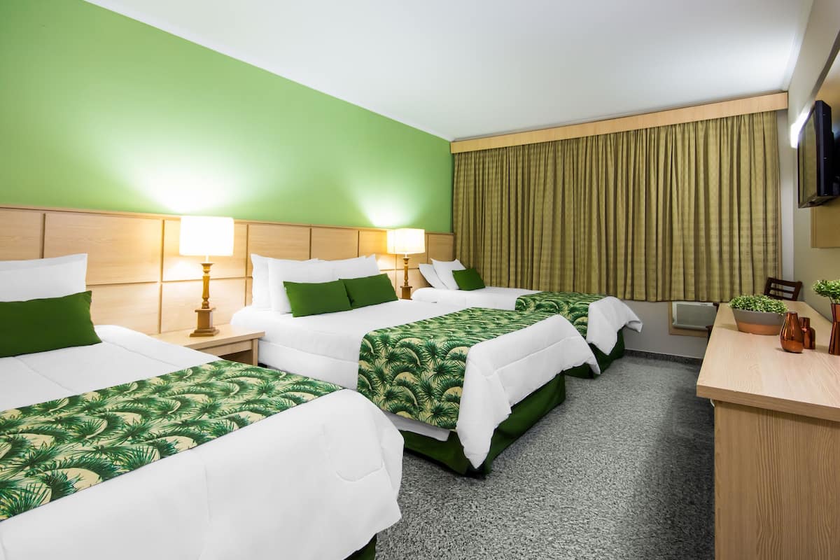 Een hotelkamer met drie bedden, groene wanden en een houten bureau met een plant.