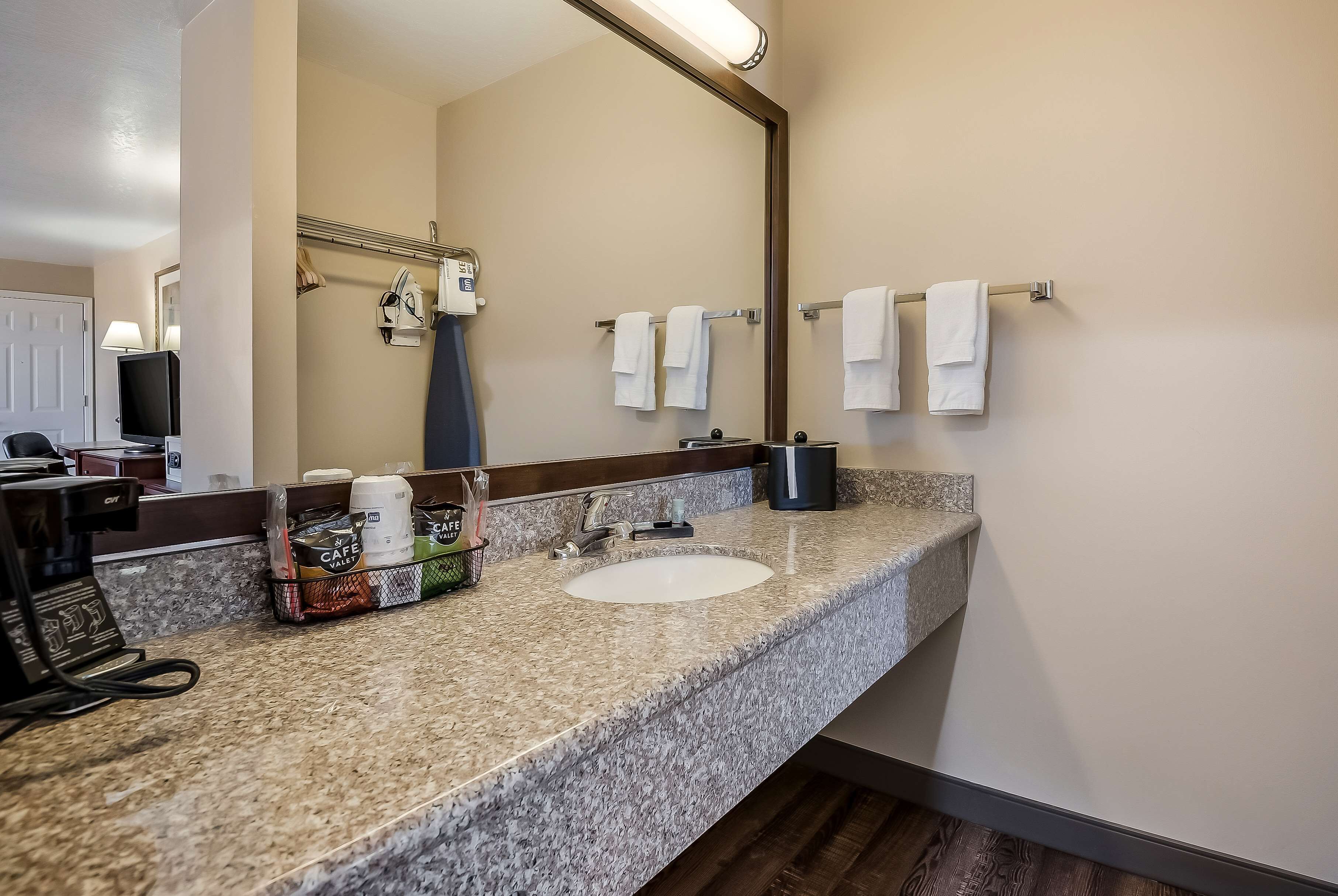 A bathroom with a granite countertop, a sink, a mirror, a towel rack, and a coffee maker.
