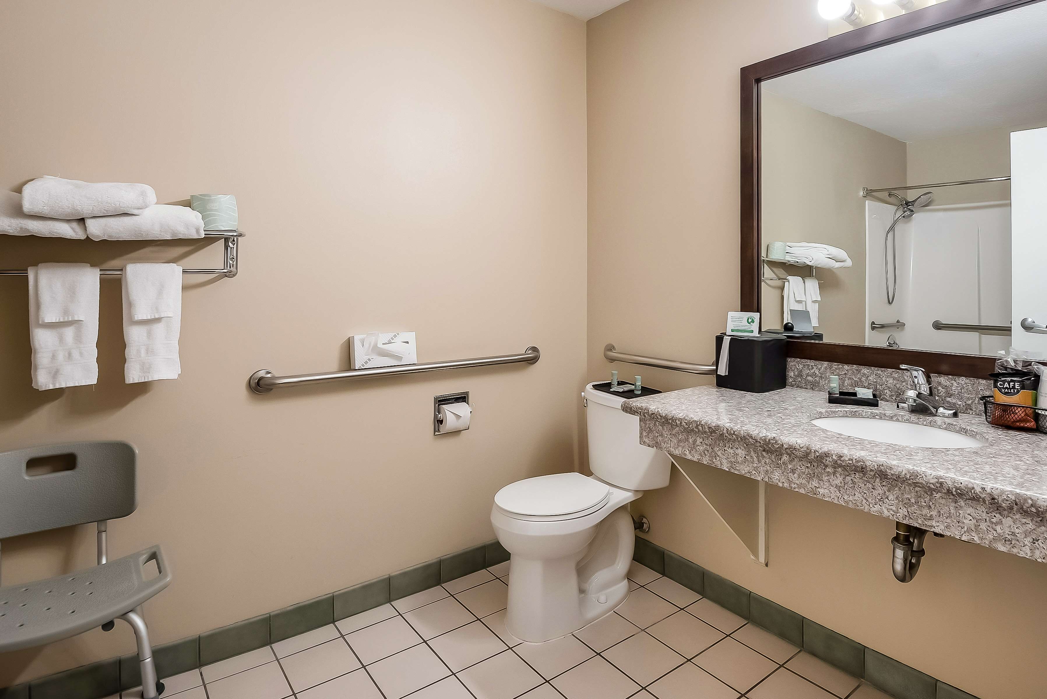 A bathroom with a toilet, sink, mirror, towel rack, and a bench.