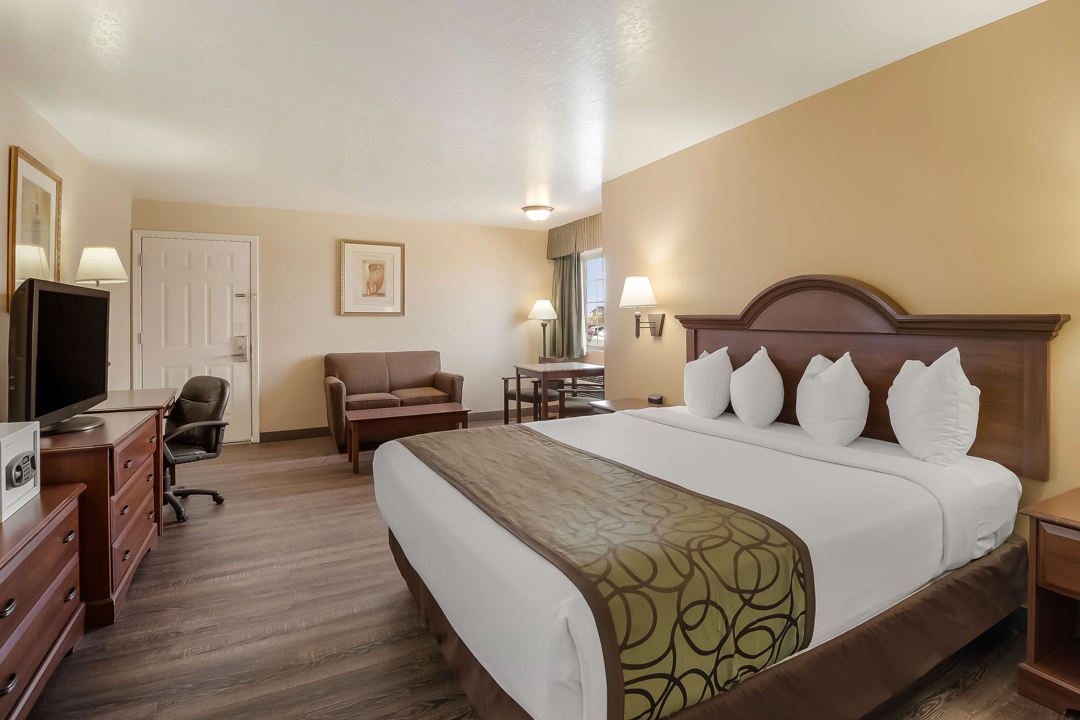 A hotel room with a large bed, a desk with a computer, a chair, a TV, and a door.