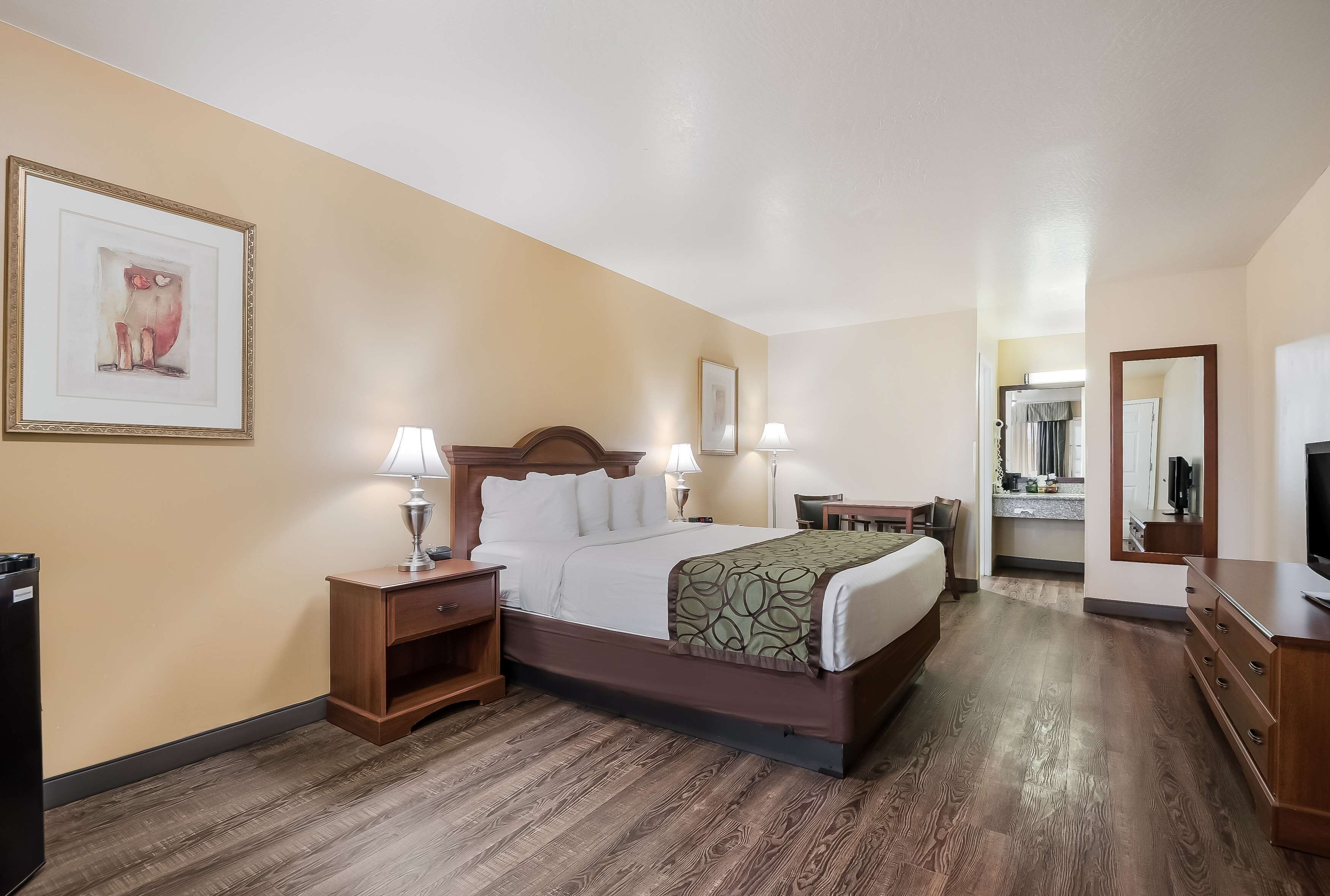 Una habitación de hotel con cama, mesitas de noche, escritorio y espejo.