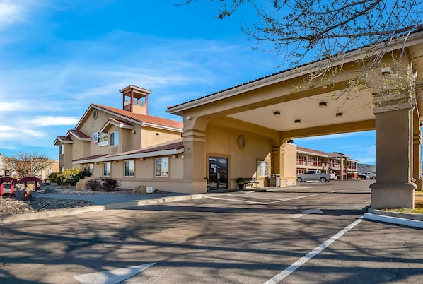 A hotel with a covered parking area, a bell tower, and a building with a red roof.