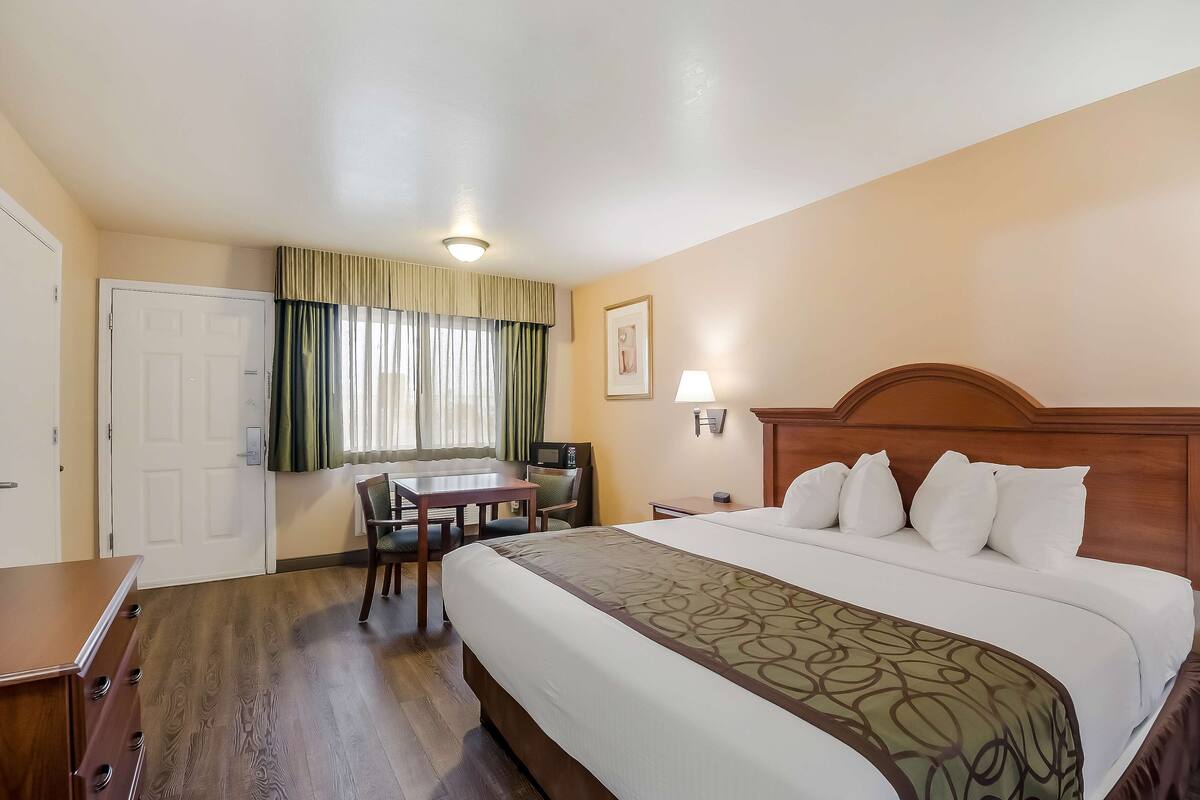 A hotel room with a large bed, a desk, a chair, a TV, and a door.