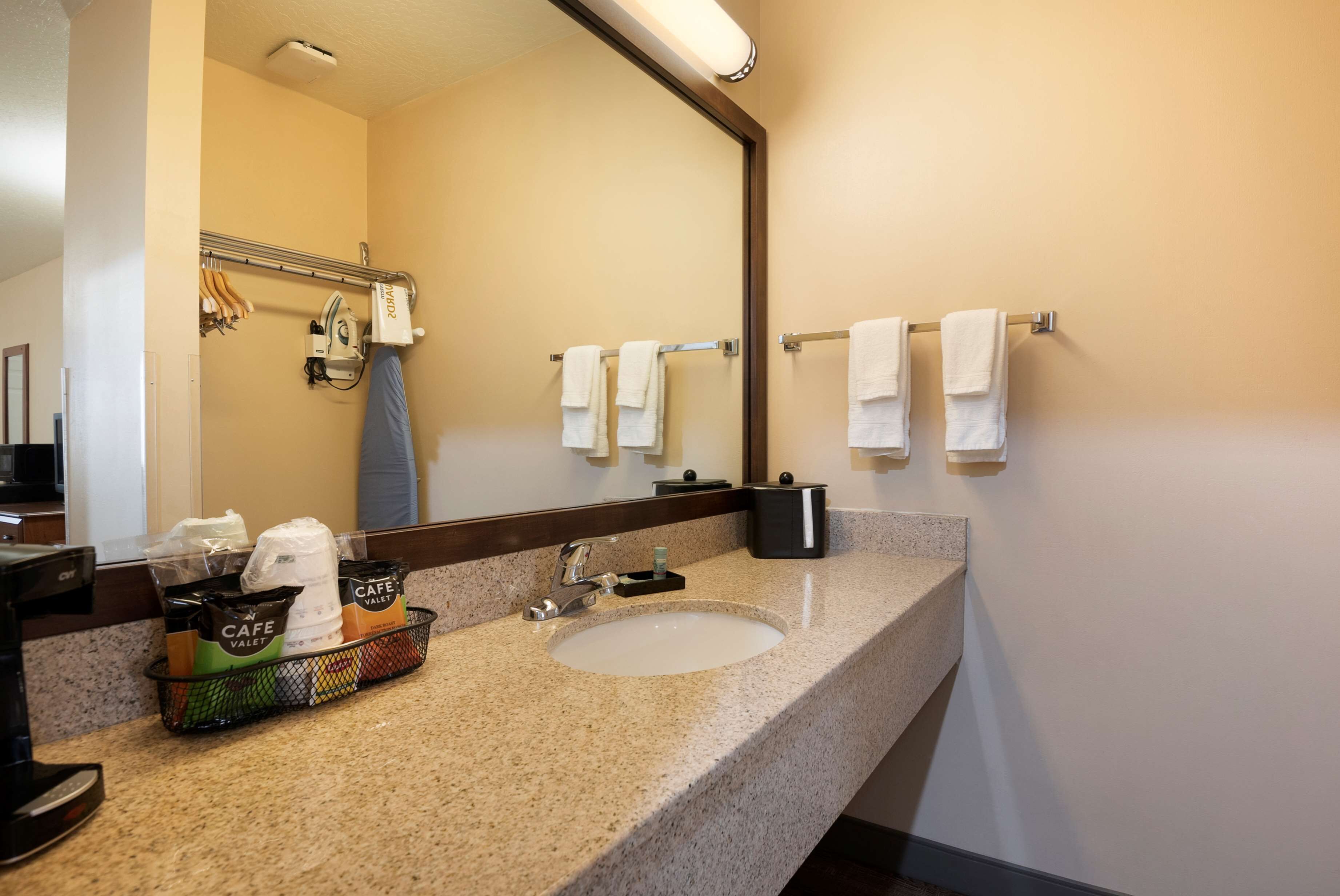 A hotel bathroom with a granite countertop, a sink, a mirror, and a towel rack.
