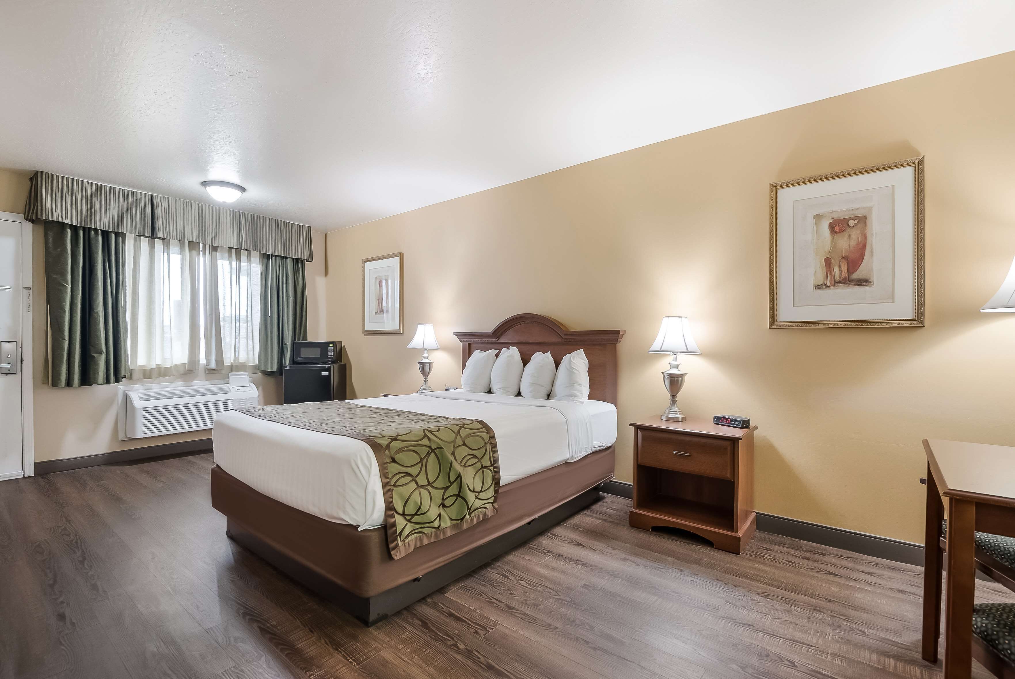Hotelkamer met een groot bed, nachtkastjes met lampen, een bureau, een stoel, een ingelijst schilderij aan de muur en een raam met gordijnen.