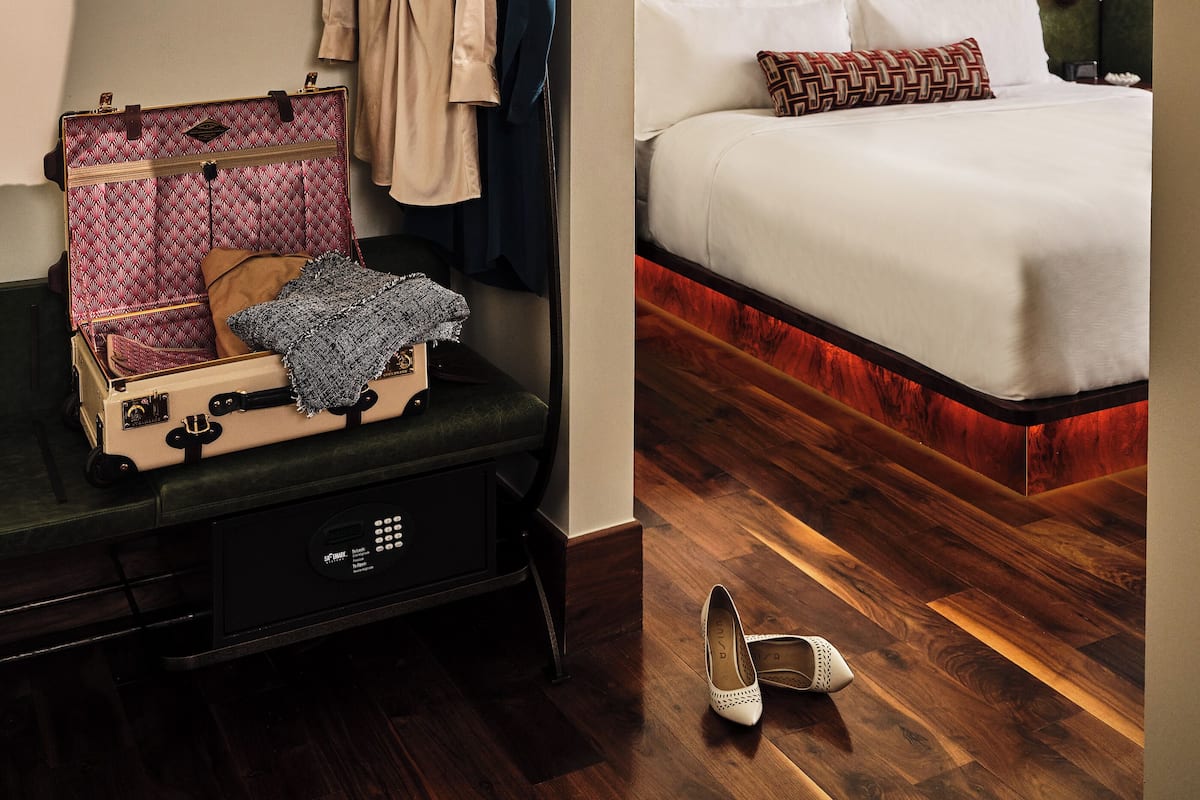 Une chambre d’hôtel avec un lit, une armoire, un porte-chapeau et une valise.