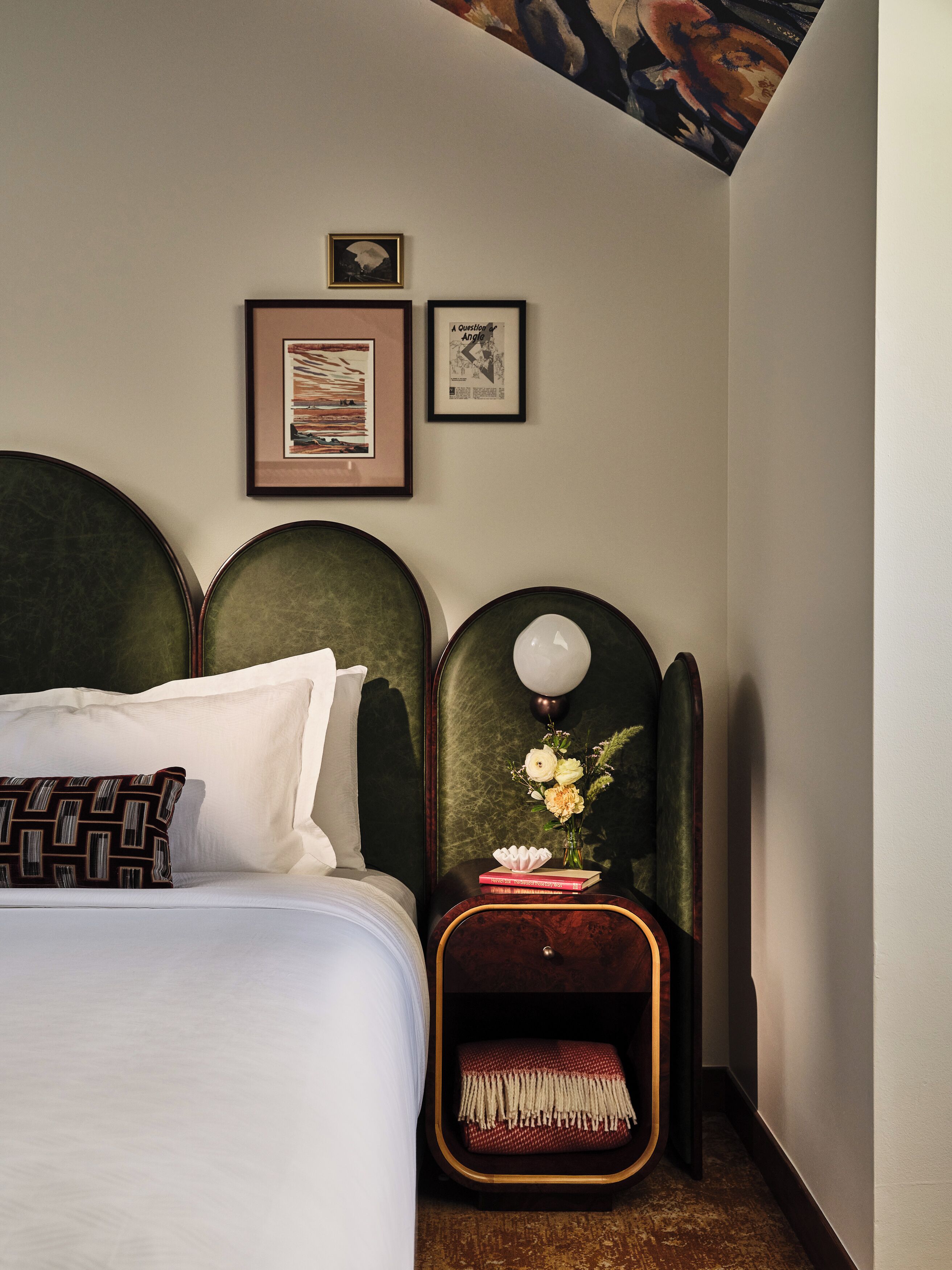 A neatly arranged bedroom with a large bed, a bedside table with a lamp, and two framed pictures on the wall.