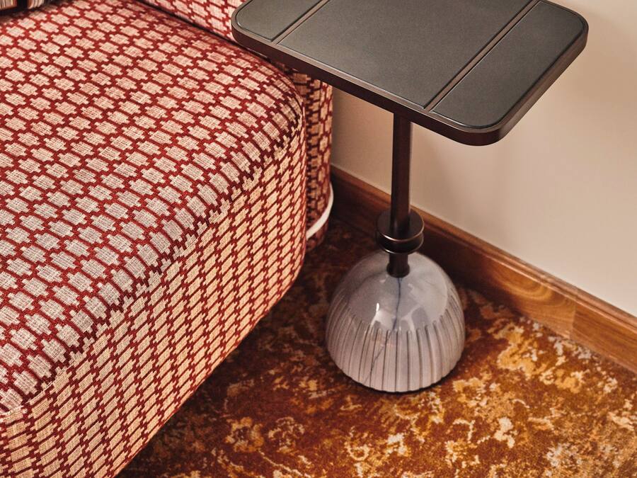 Esquina de una habitación con un sofá estampado y una pequeña mesa negra con patas blancas.