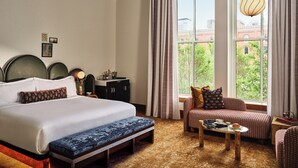 A hotel room with a large bed, a bench, a sofa, a coffee table, and a view of greenery through the window. - The Crawford Hotel (Denver)