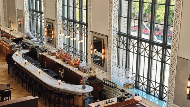 A spacious bar area with high ceilings and large windows, offering views of the cityscape. - The Crawford Hotel (Denver)