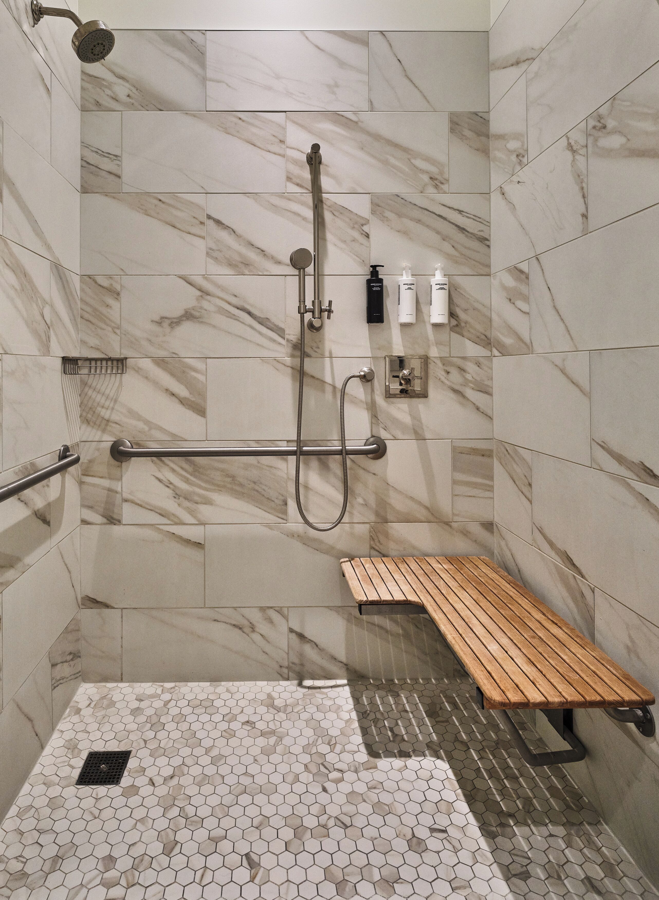 A shower area with a wooden bench, marble tiles, and a hand shower.