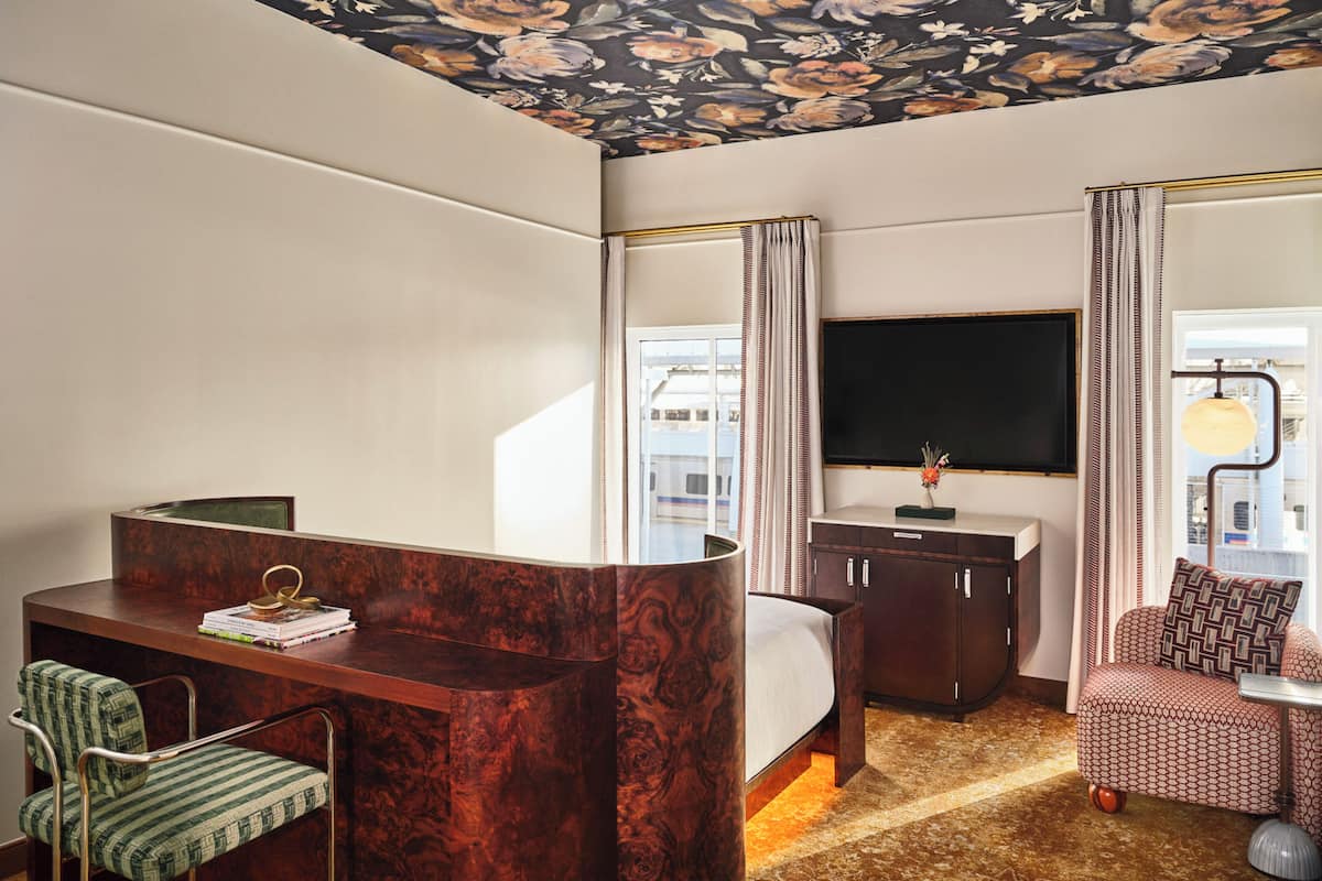 Une chambre d’hôtel avec un lit, un bureau, une chaise, une télévision et une fenêtre avec des rideaux.