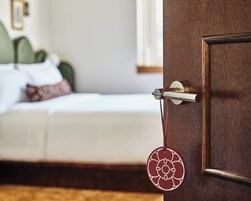 A wooden door with a brass handle and a keyhole, a circular decorative item hanging from the handle, and a bed with white bedding and pillows in the background.