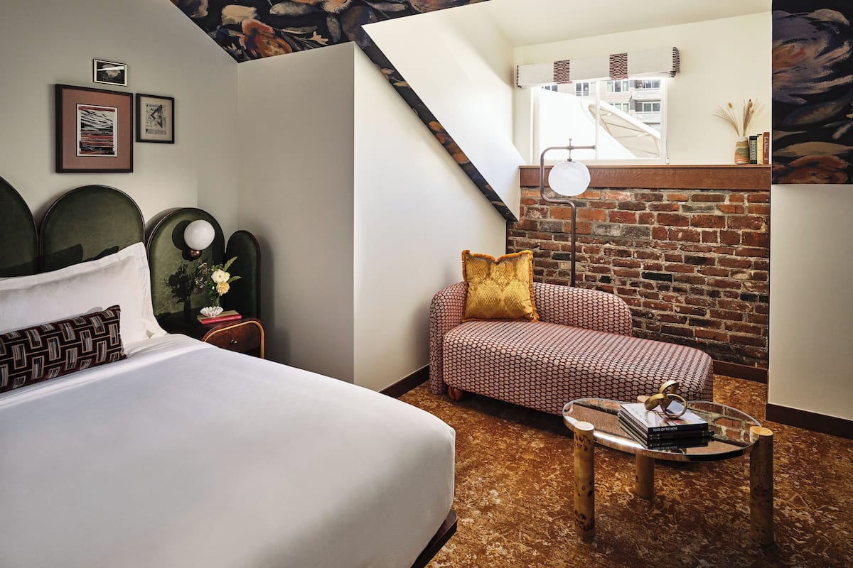 Une chambre d’hôtel avec un lit, un canapé, une petite table avec des livres, une lampe et un mur en briques.