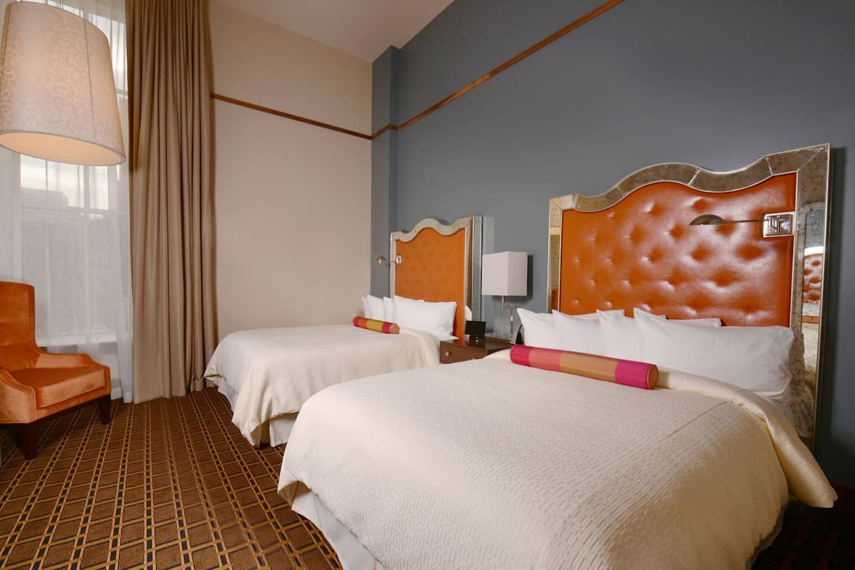 Une chambre d’hôtel avec deux lits, une chaise, une lampe et un sol à motifs.