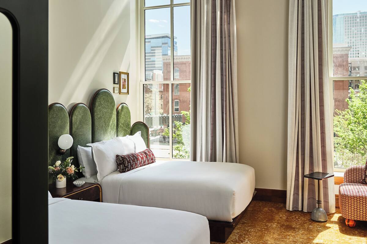 Une chambre d’hôtel avec deux lits, une vue sur la ville et une petite table avec une lampe.
