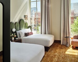 Habitación de hotel con dos camas, vista a la ciudad y una pequeña mesa con lámpara.