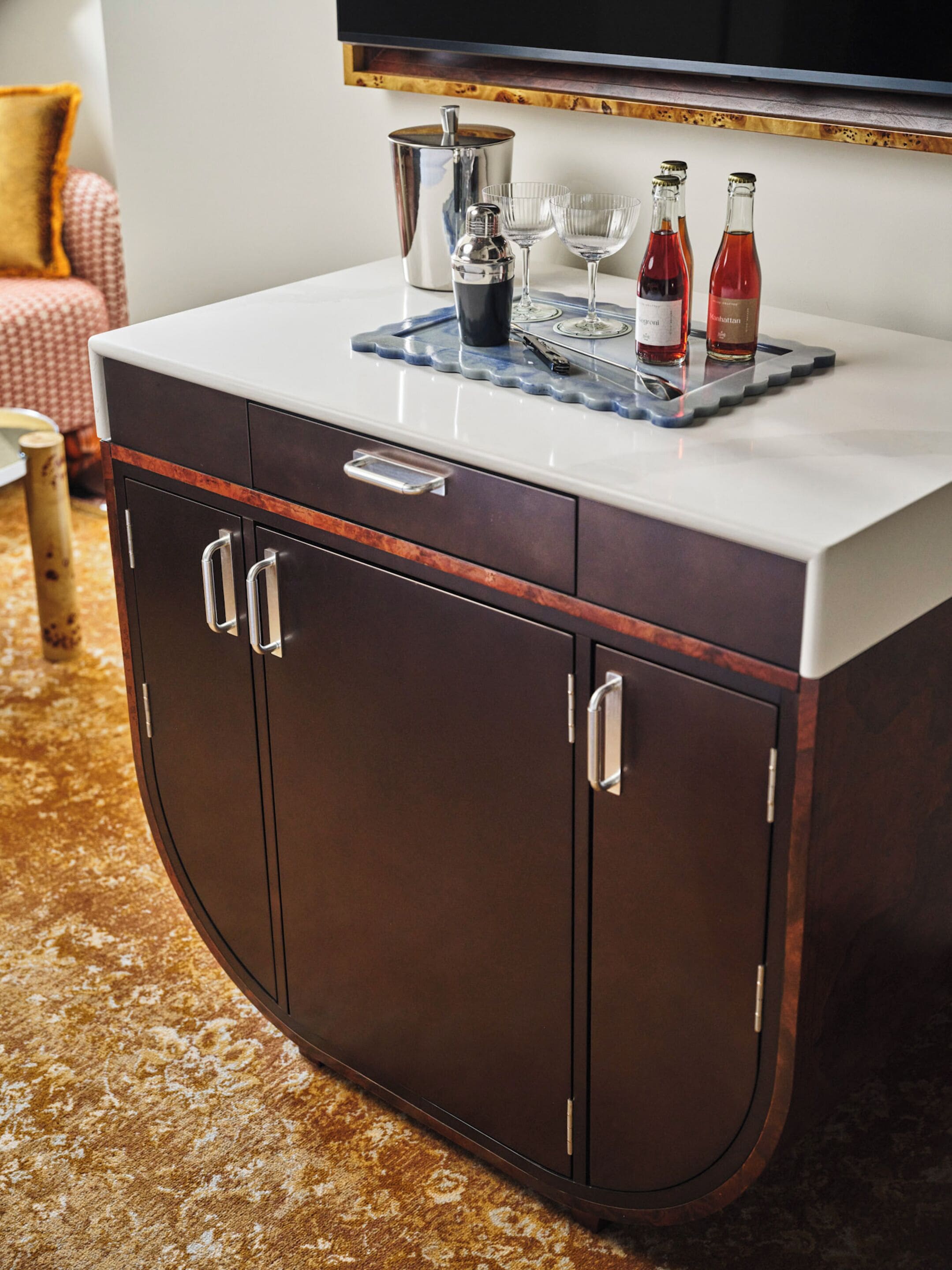 Un mueble de madera oscura con una encimera blanca, un shaker de cócteles y dos botellas sobre una bandeja.