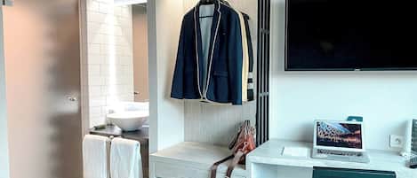Ein modernes Badezimmer mit einem weißen Waschbecken, einem Handtuchhalter mit mehreren Handtüchern, einem aufgehängten Mantel und einem Laptop auf einem Schreibtisch.