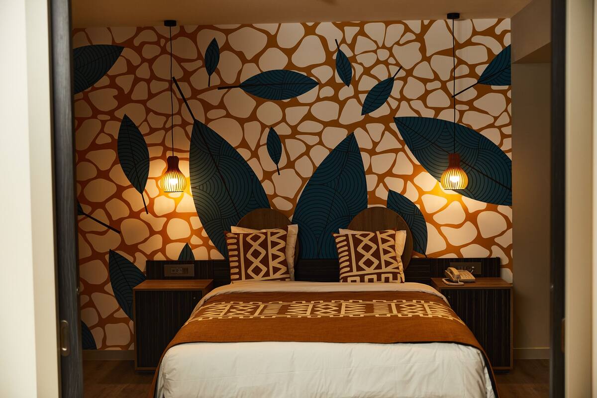 Een slaapkamer met een behang met patroon, een bed met een bruine deken, twee nachtkastjes met lampen, en een bijzettafeltje met een telefoon.