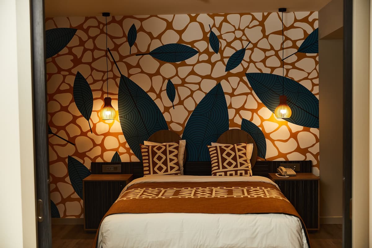 Un dormitorio con una pared estampada, una cama con manta marrón, dos mesitas de noche con lámparas y un aparador con teléfono.