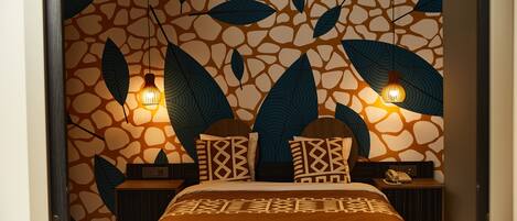 Un dormitorio con una pared estampada, una cama con manta marrón, dos mesitas de noche con lámparas y un aparador con teléfono.