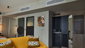 A modern living room with a yellow sofa, geometric patterned pillows, and a wall-mounted abstract art piece.