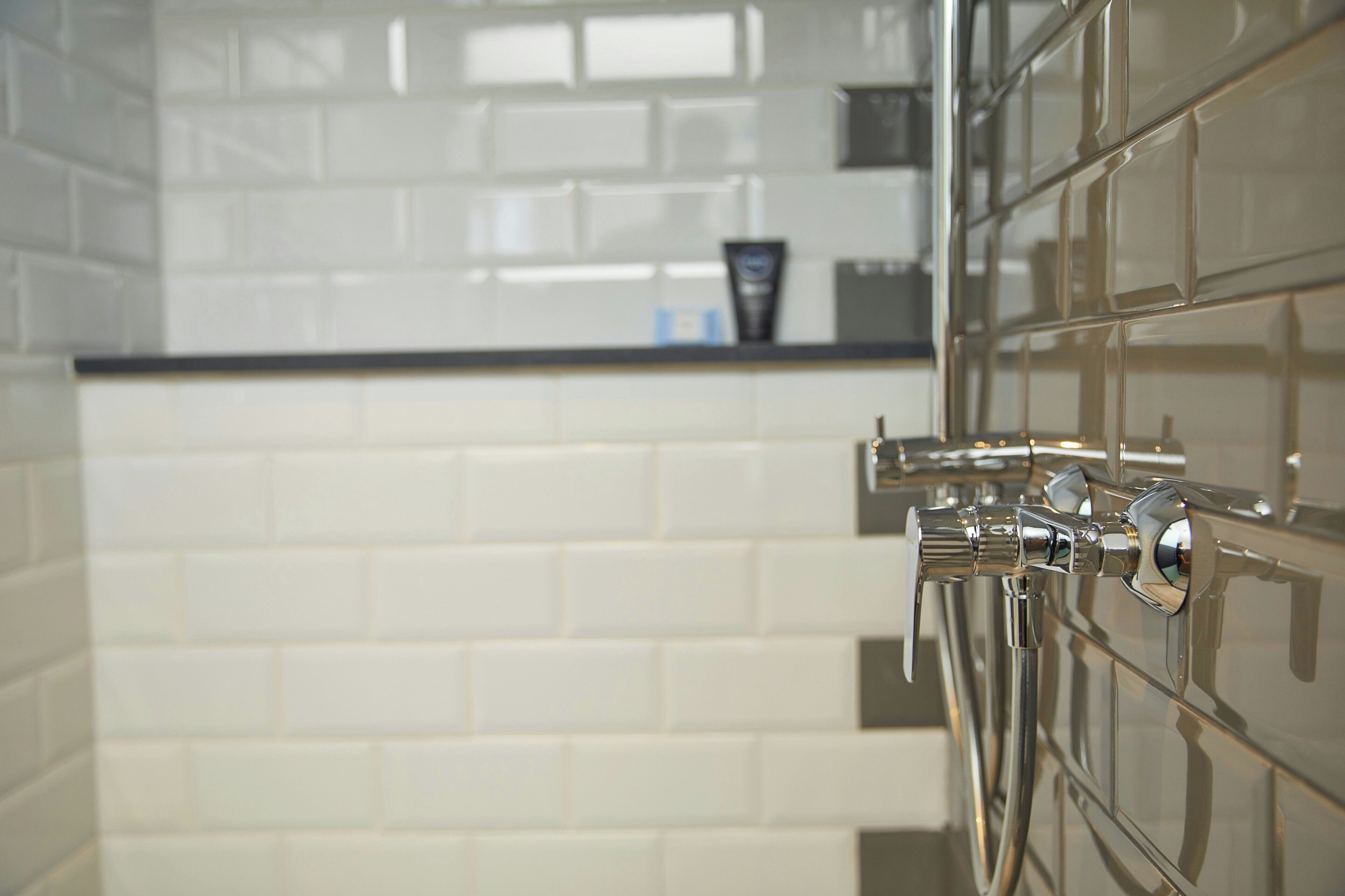A bathroom with white tiled walls and a chrome faucet.