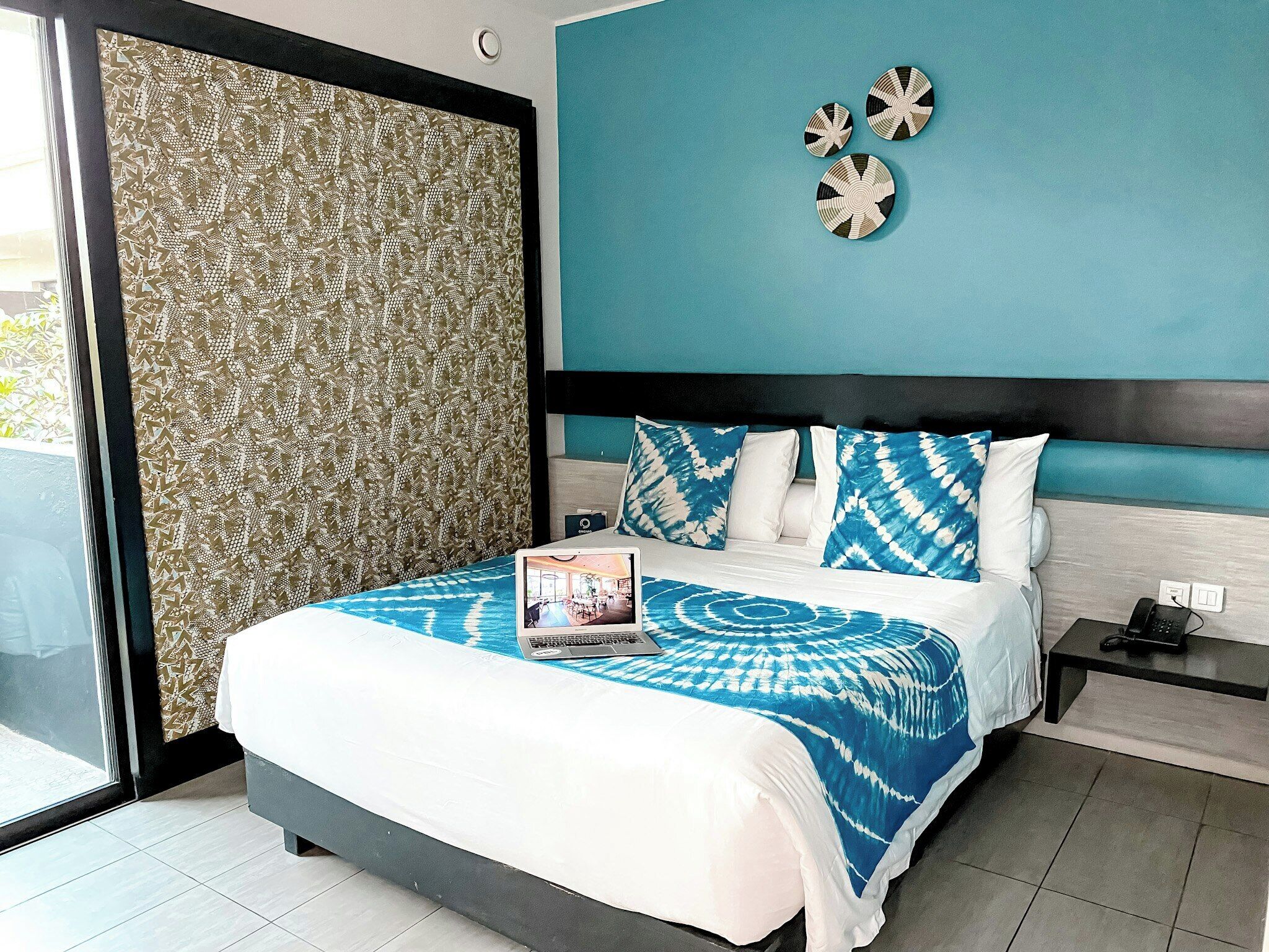 A hotel room with a bed, a nightstand, a wall clock, and a window with a view.