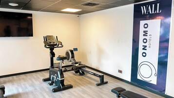 Un gimnasio con equipamiento de ejercicio, una banca y un gran anuncio en la pared para Wall Nommo Hotels.