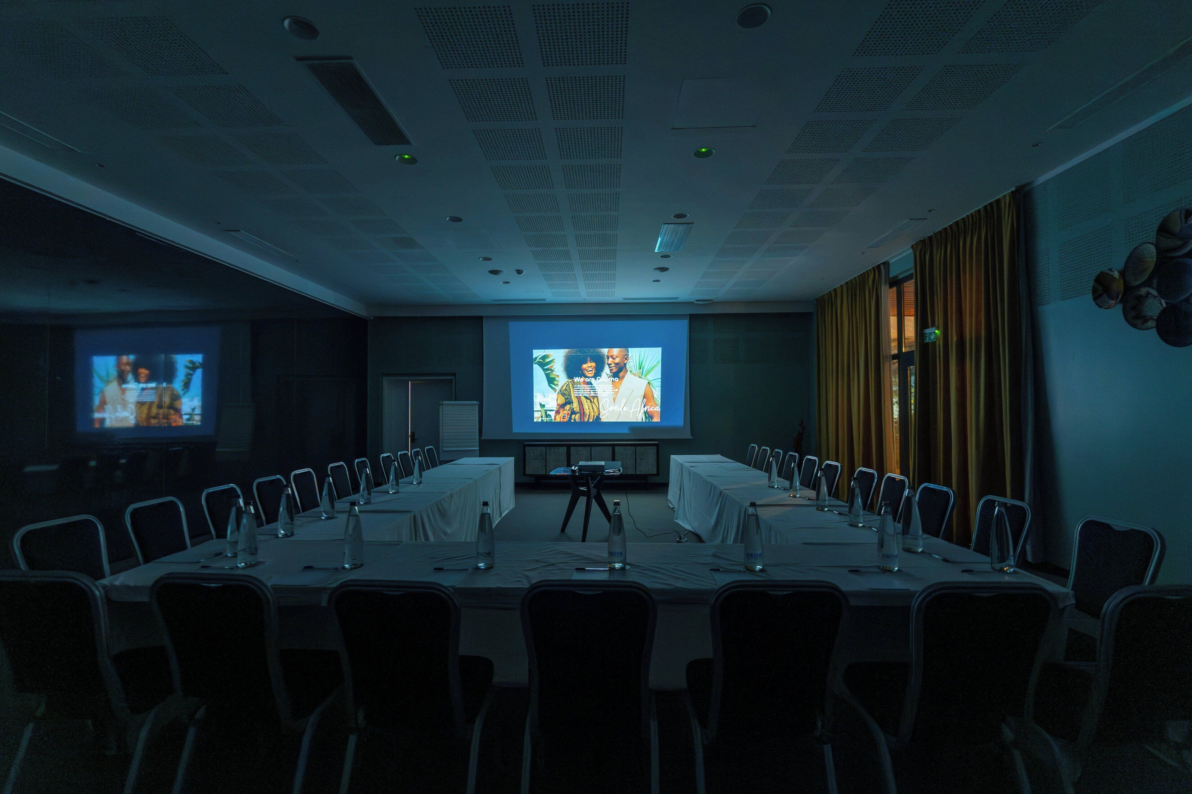 A conference room with a long table, chairs, a projector screen, and a presentation screen.