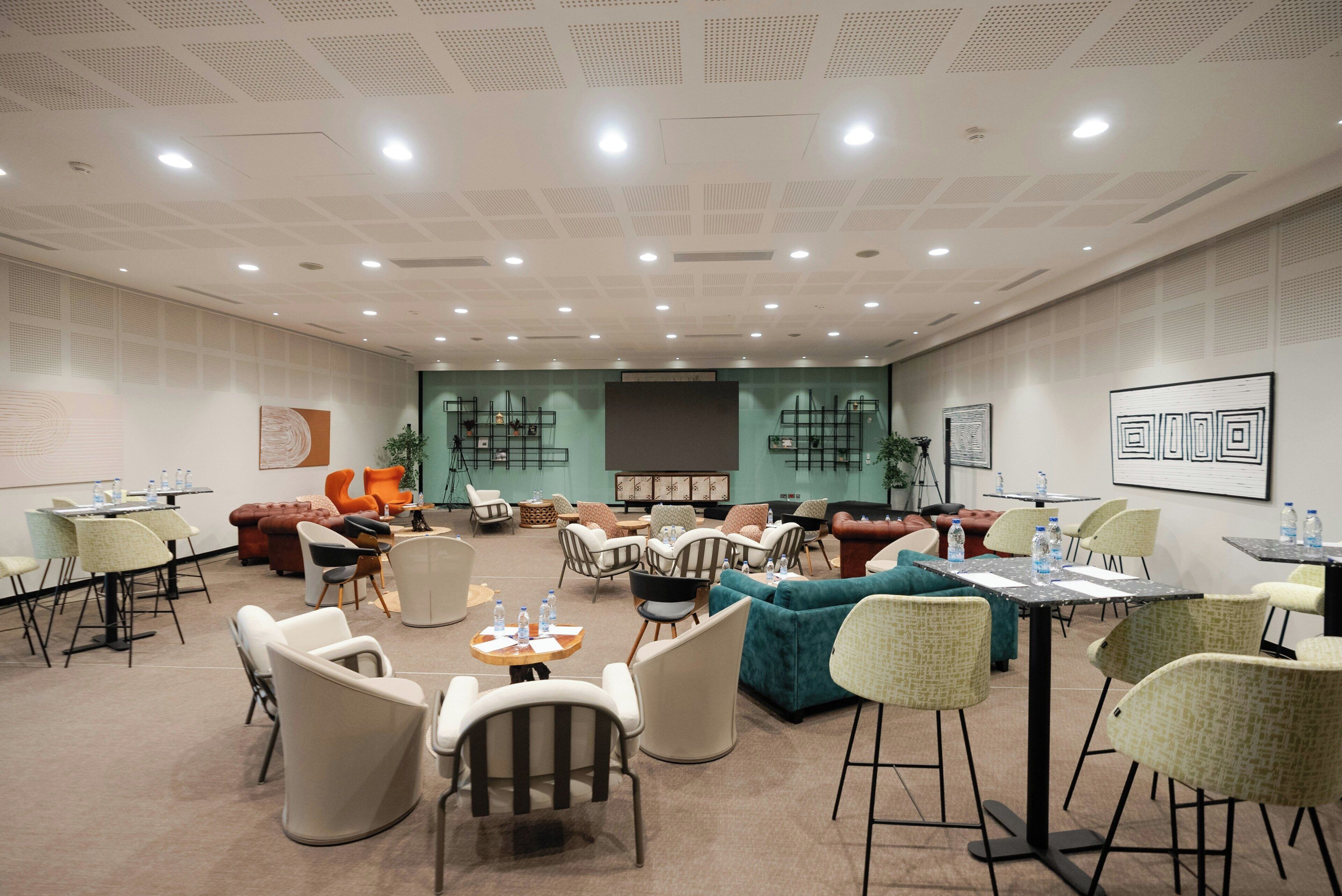 A conference room with multiple tables and chairs, a stage, and a seating area with sofas and armchairs.