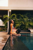 Una pareja junto a una piscina, con palmeras al fondo.