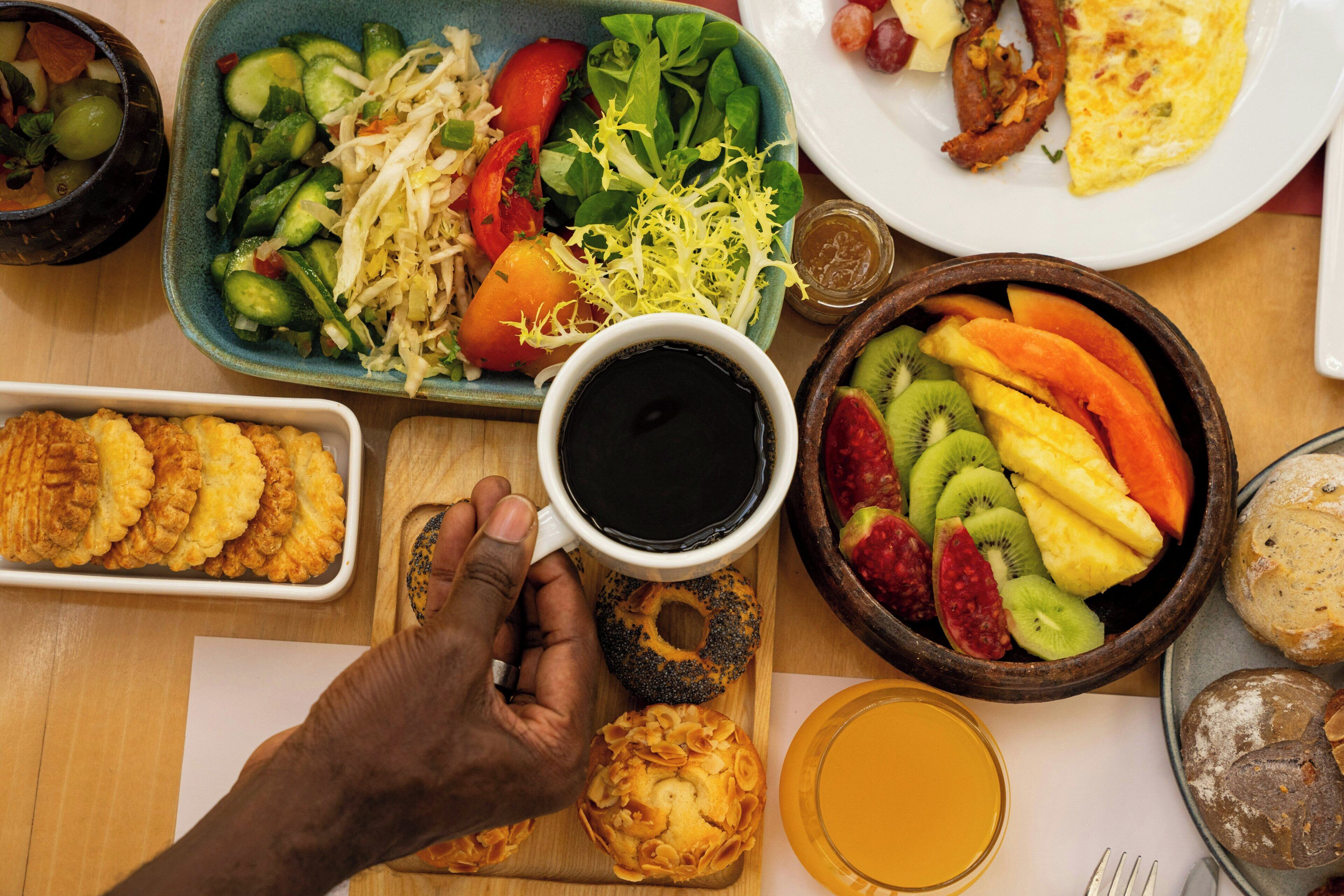 A breakfast setting with various dishes, a cup of coffee, and a bowl of fruit.