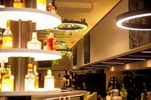 Een barruimte met meerdere hangende lampen, drankflessen en een zithoek.