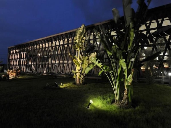 Un edificio moderno con fachada geométrica y un jardín bien cuidado con plantas de hojas grandes.
