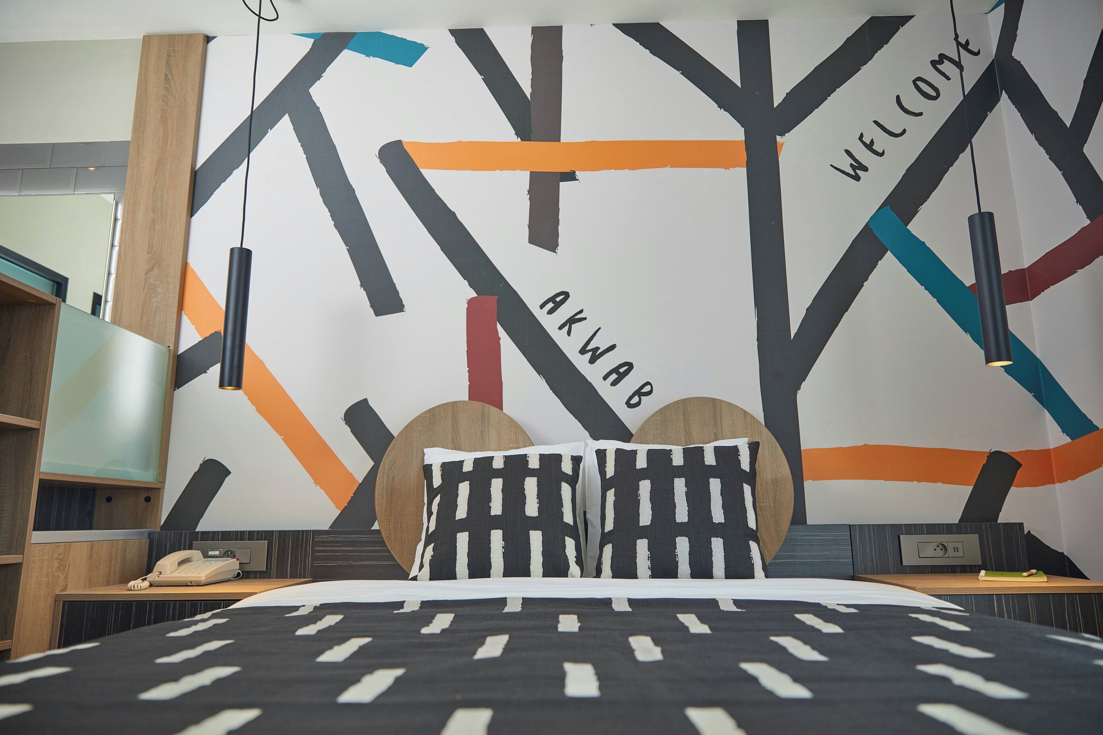 A modern hotel room with a bed, a desk, a telephone, and a wall with abstract art.