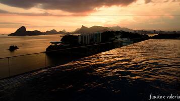 Un paisaje urbano costero al atardecer, con vista al océano, edificios y montañas al fondo.