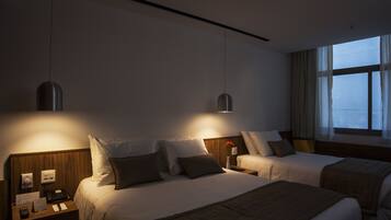 Habitación de hotel con dos camas, cabecero de madera, mesitas de noche con lámparas y una ventana con cortinas.