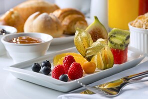 Una bandeja de desayuno con croissants, frutas y un tazón pequeño de mermelada.
