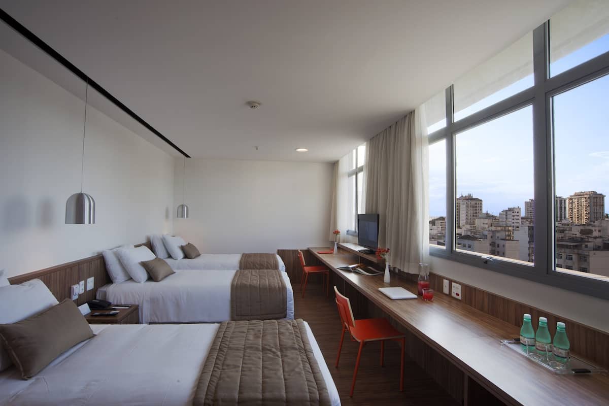 A hotel room with two beds, a desk, a TV, and a window with a city view.
