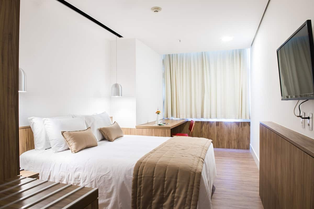 A modern hotel room with a large bed, bedside table, and a TV mounted on the wall.